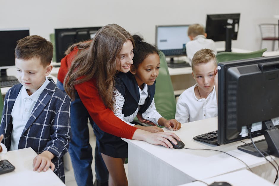 Teacher engaging with diverse children in a technology lesson using computers in a modern classroom.